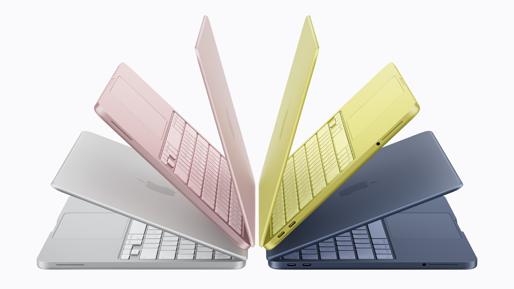 Four Apple laptops (the new MacBook Neo) with a thin-and-light aluminum design, shown from the side and slightly above, arrayed in a fan shape slightly open so you can see their keyboards and trackpads. Each is a different color—silver, pink, yellow, and dark blue.